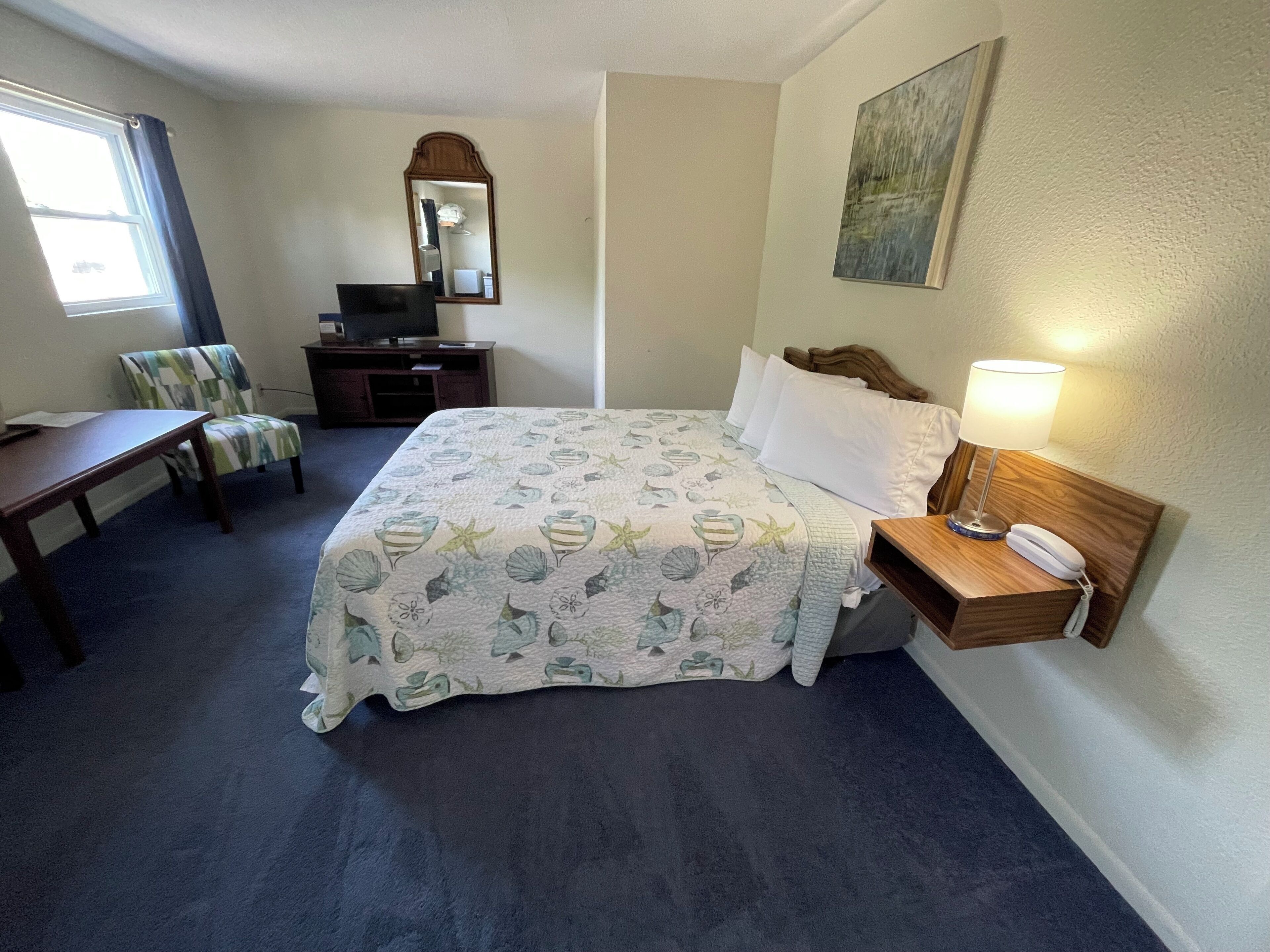 Een hotelkamer met een bed, een bureau, een stoel, een televisie, een spiegel en een lamp.