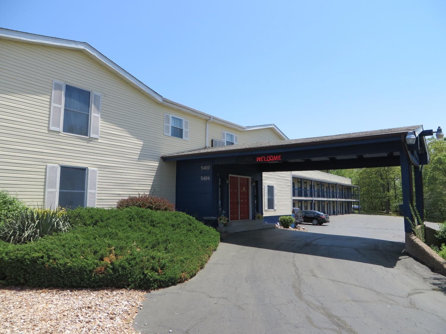A motel with a covered entrance, numbered units, and a parking area.