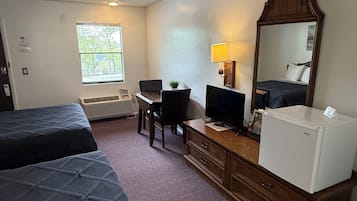 A hotel room with two beds, a desk with a computer, a refrigerator, a mirror, and a window with blinds.