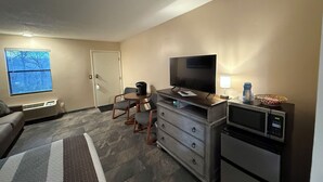 A compact hotel room with a flat-screen TV, a microwave, a small refrigerator, a sofa, and a dining table with chairs. - The No Wake Inn - Osage Beach (Osage Beach)
