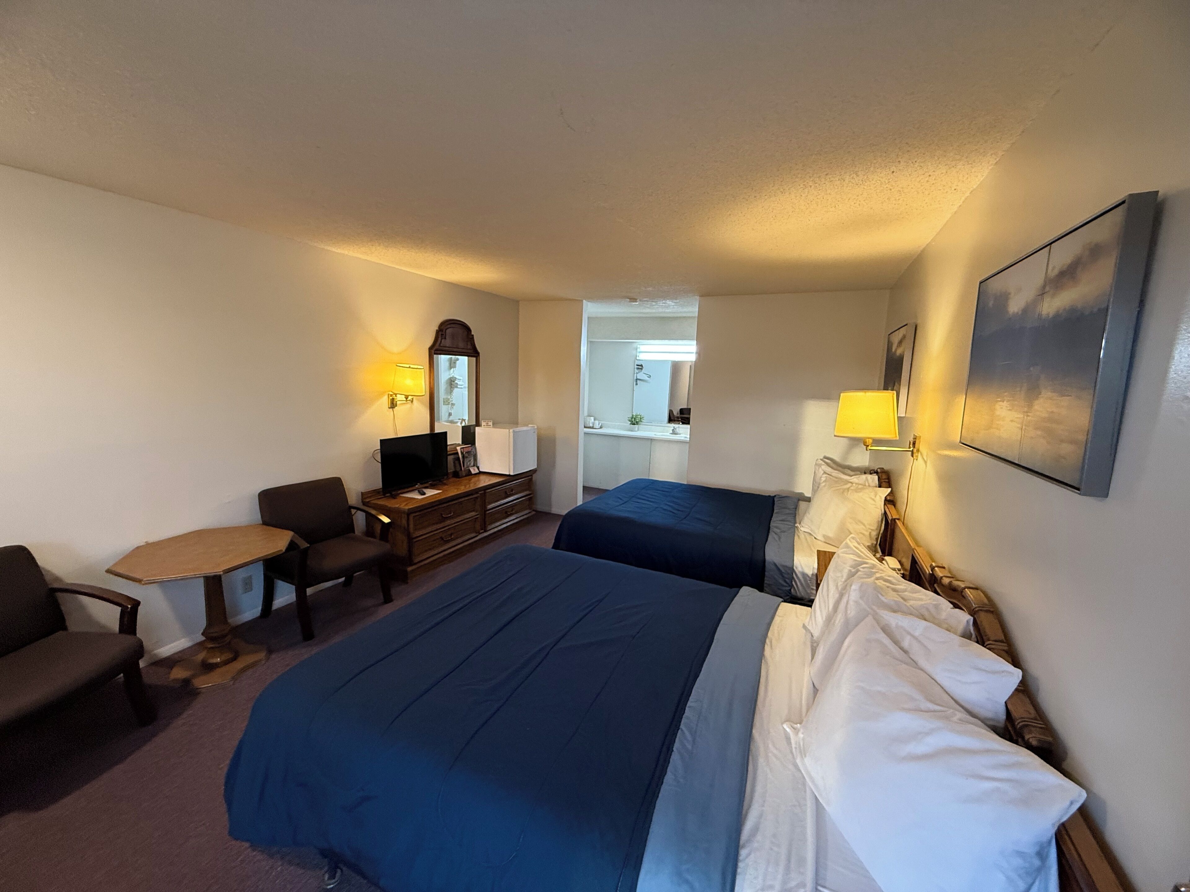 Ein Hotelzimmer mit zwei Betten, einem Schreibtisch, einem Stuhl, einer Kommode und einem Fernseher.