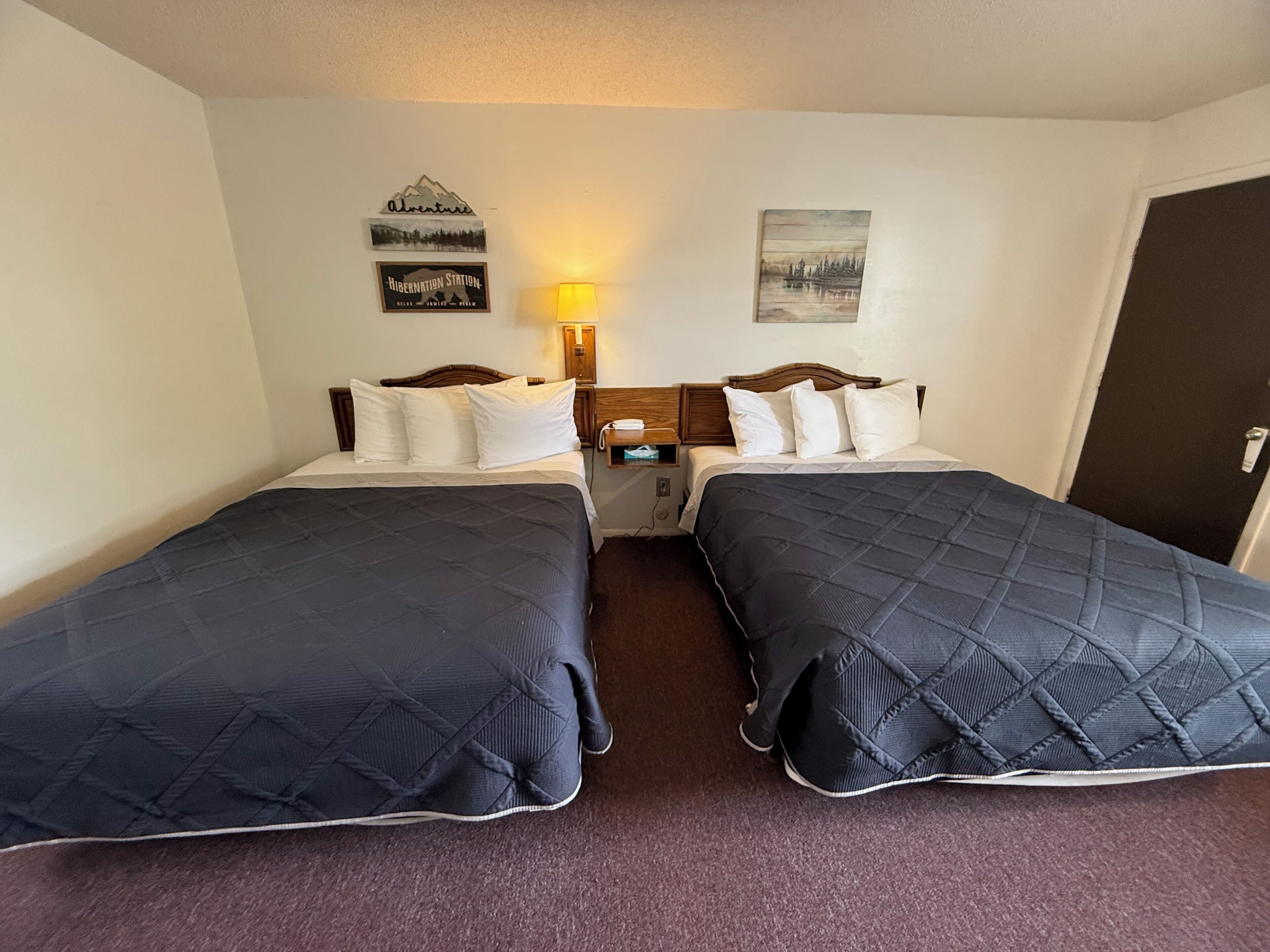 Una habitación de hotel con dos camas, una mesita de noche, una lámpara y decoración en la pared.