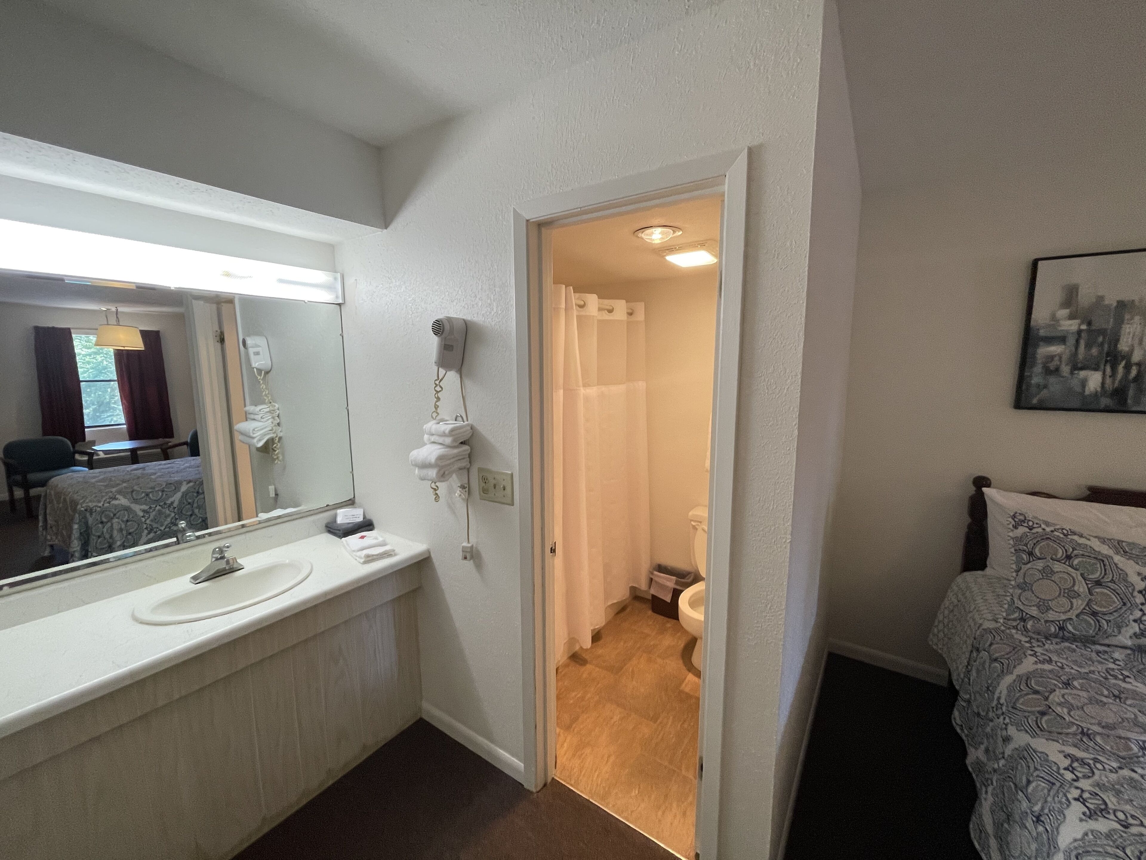 Une salle de bain d’hôtel équipée d’un grand miroir, d’un lavabo, d’un sèche-cheveux et d’une douche.