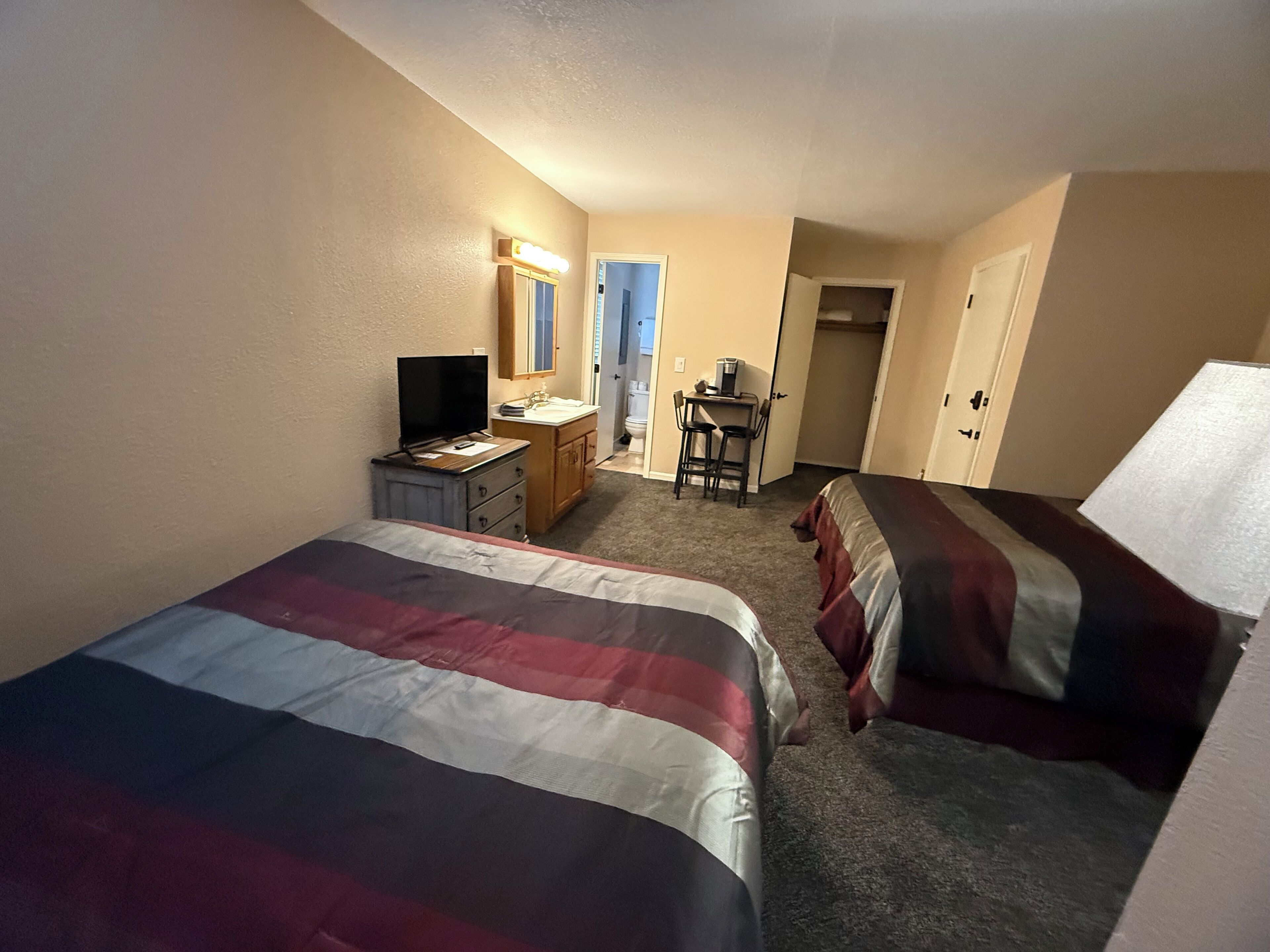 Ein Hotelzimmer mit zwei Betten, einem Schreibtisch mit Computer, einem Sessel und einem kleinen Tisch mit Kaffeemaschine.