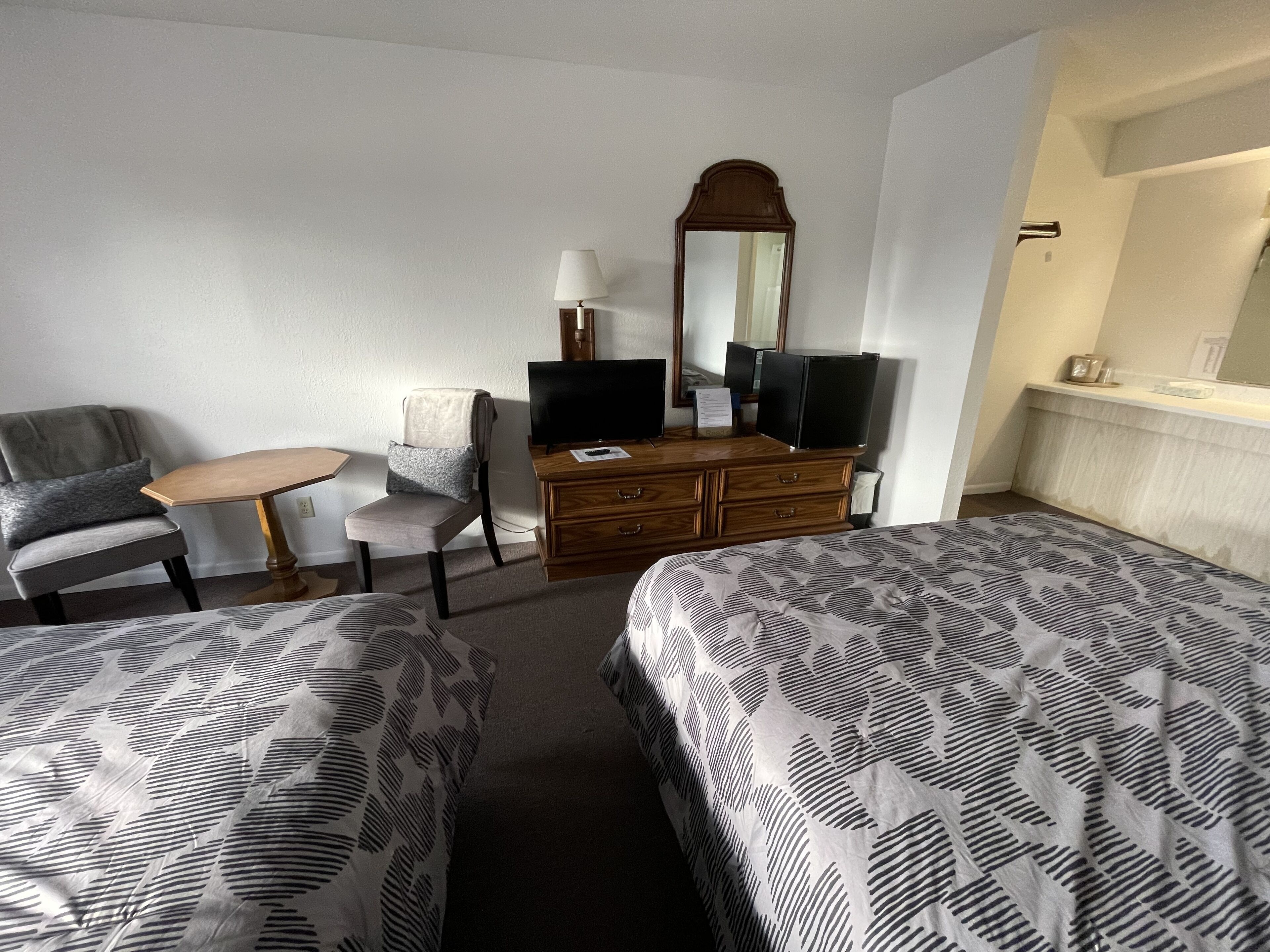 A hotel room with two beds, a desk, a chair, a dresser, a television, and a mirror.
