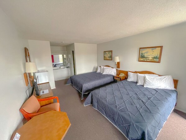 A hotel room with two beds, a desk, a chair, a lamp, and a painting on the wall.