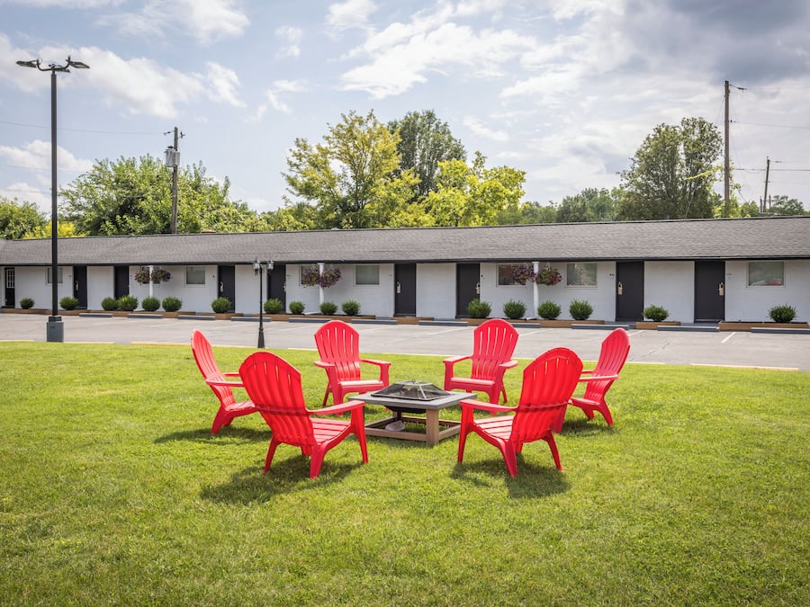 A motel with a row of rooms, a grassy lawn, and red chairs around a fire pit.