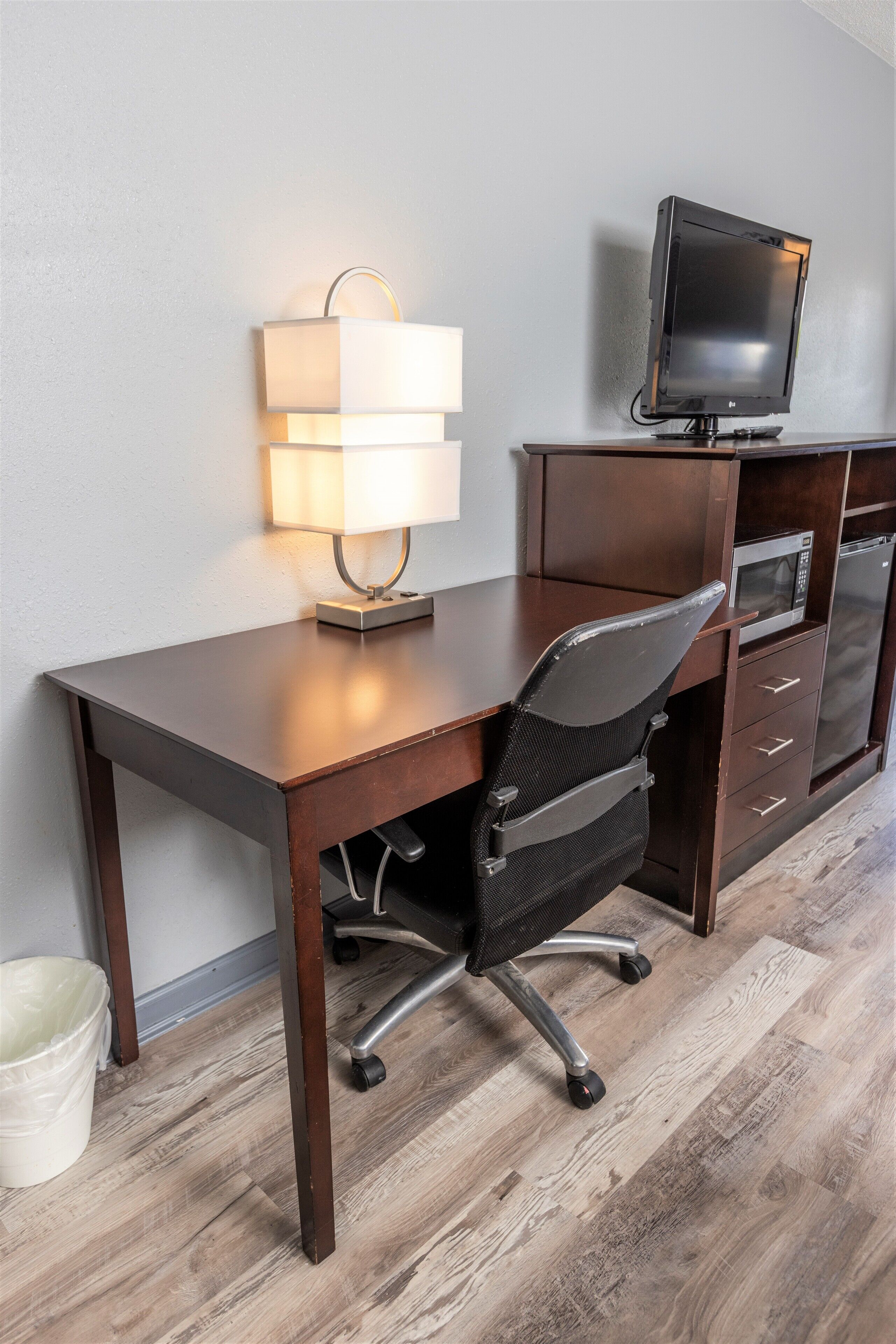 A modern office desk with a lamp, a chair, a television, and a microwave.