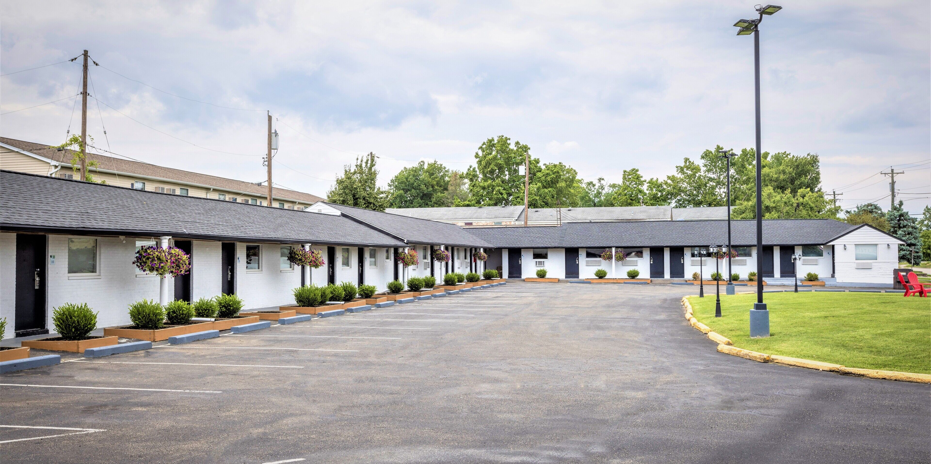 Ein Motel mit einer Reihe von Zimmern, einem Parkplatz und einer Rasenfläche mit einem roten Stuhl.