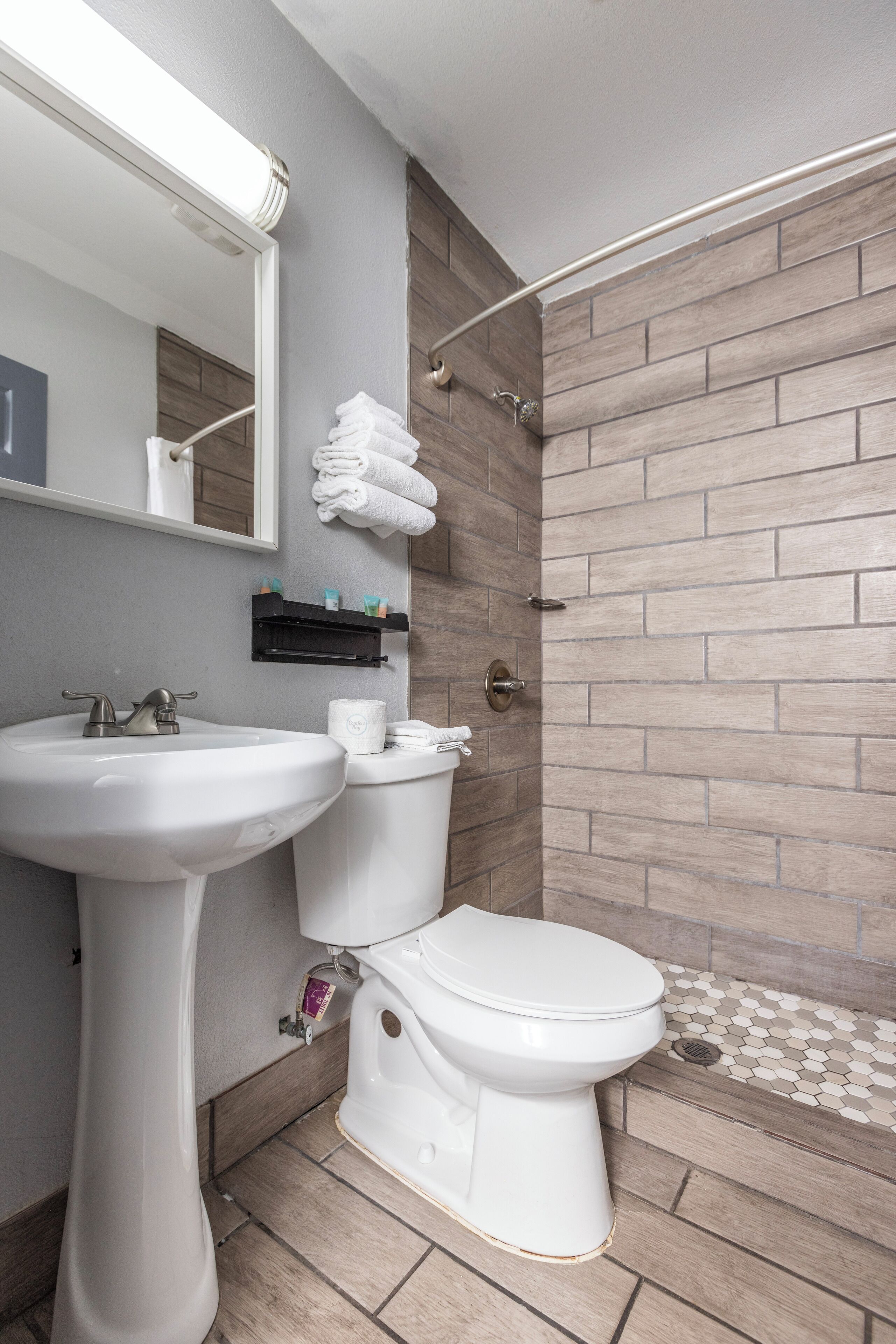 Een badkamer met een wit wastafelmeubel, toilet en douche. Boven de wastafel hangt een spiegel en er is een handdoekrek met handdoeken.
