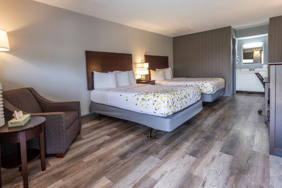 A hotel room with two beds, a chair, a small table, and a kitchenette.