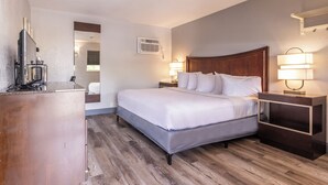 Quarto de hotel com uma cama grande, luminárias laterais, uma mesa com cafeteira e um espelho.