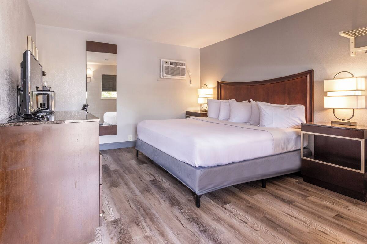 A hotel room with a large bed, bedside lamps, a desk with a coffee maker, and a mirror.