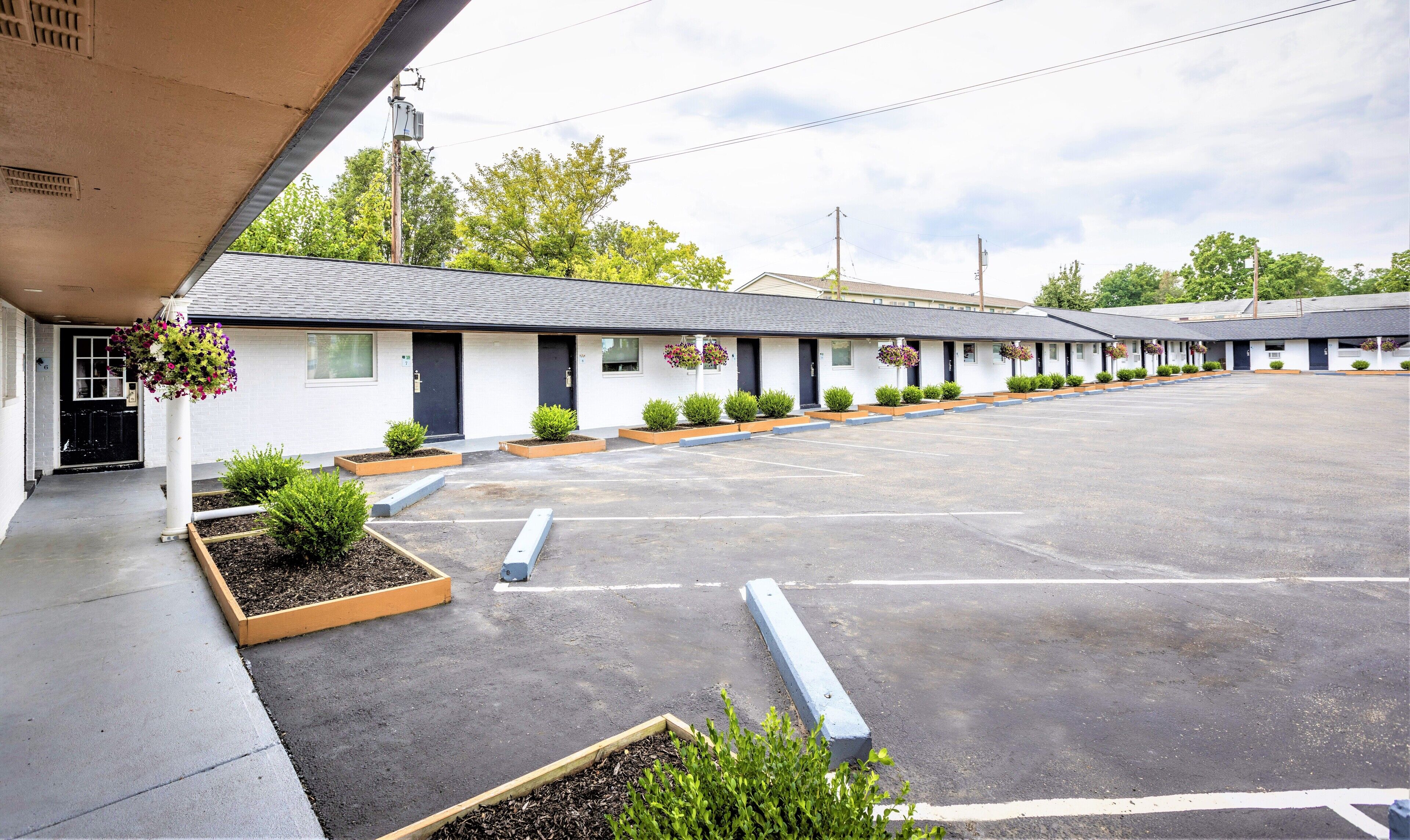 A motel with a row of rooms, a parking lot, and small planters with flowers.