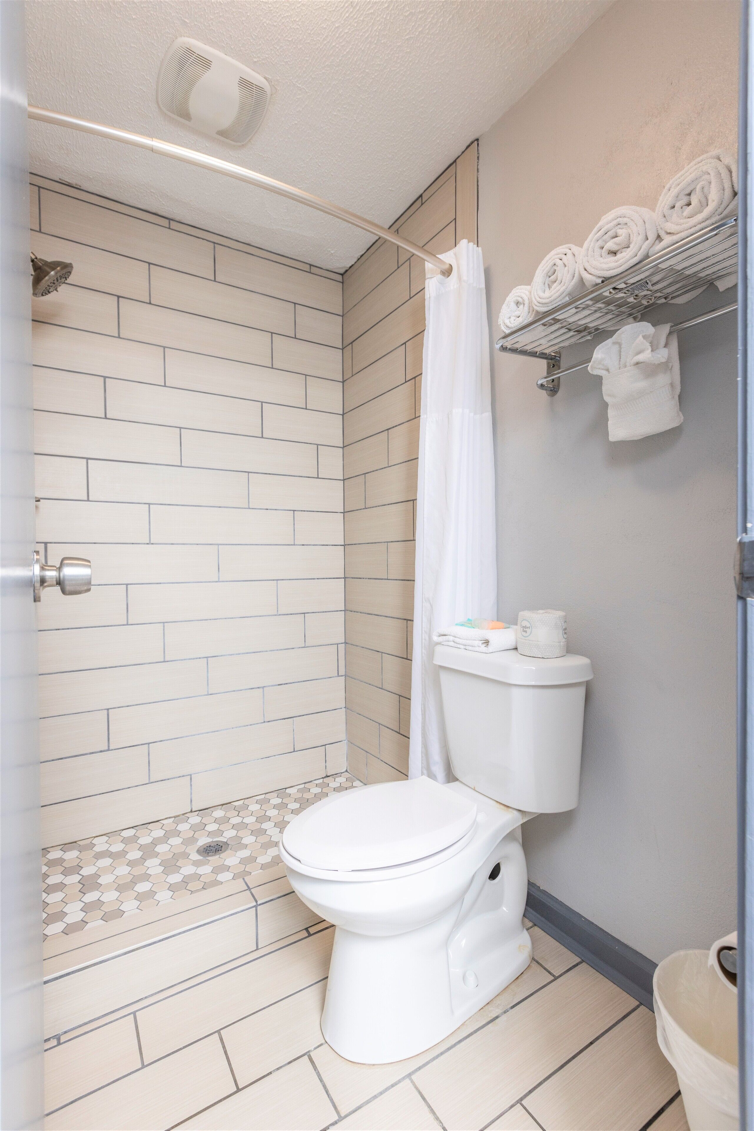 A modern bathroom with a shower, toilet, and a towel rack with neatly rolled towels.