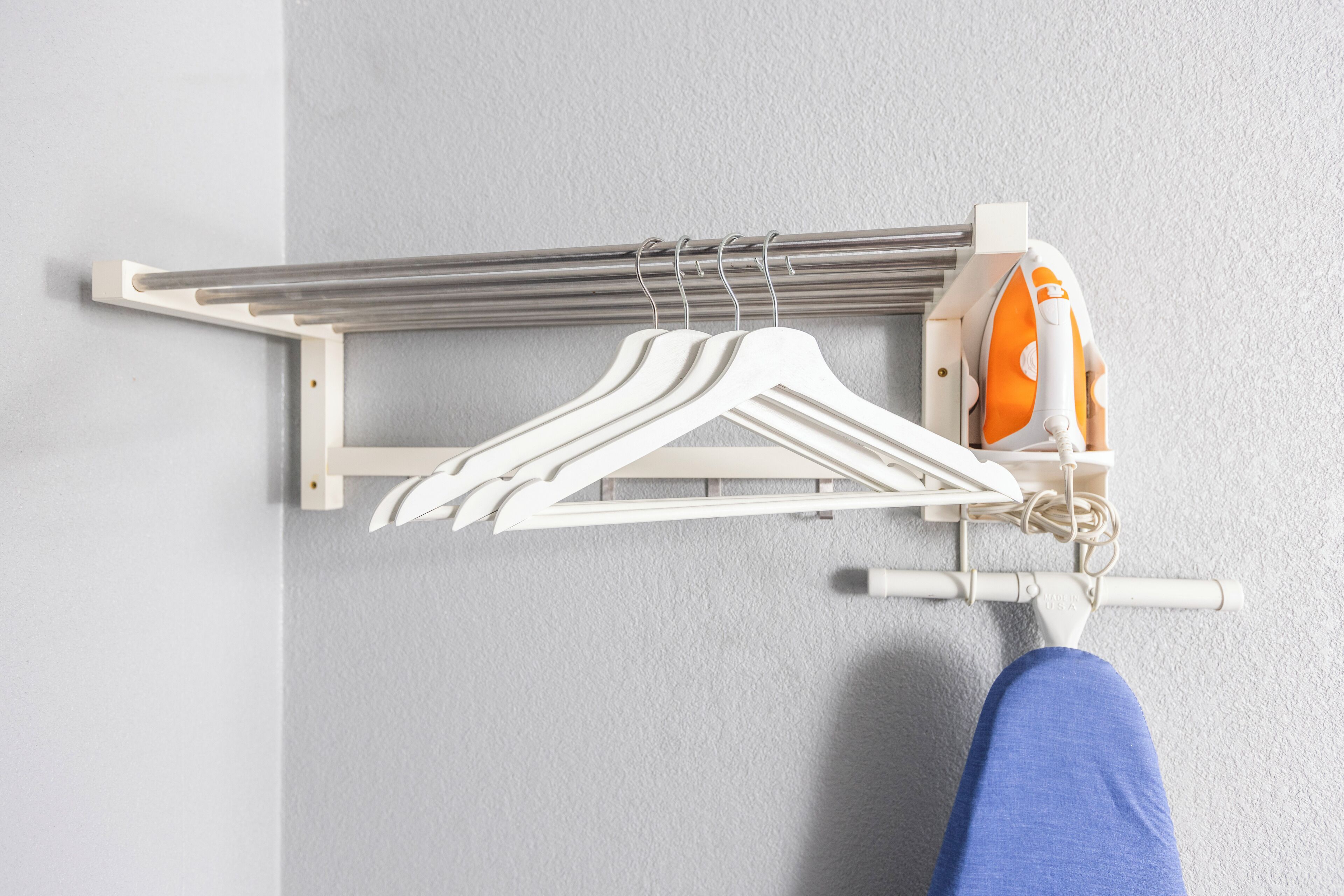 A wall-mounted drying rack with multiple hangers and a small ironing board with an iron.
