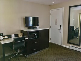 Habitación de hotel con televisión de pantalla plana, microondas, cafetera, escritorio con silla y un espejo grande.