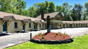 A row of motel-style buildings with a central statue in a landscaped area. - Scottish Inns Milford (Milford)