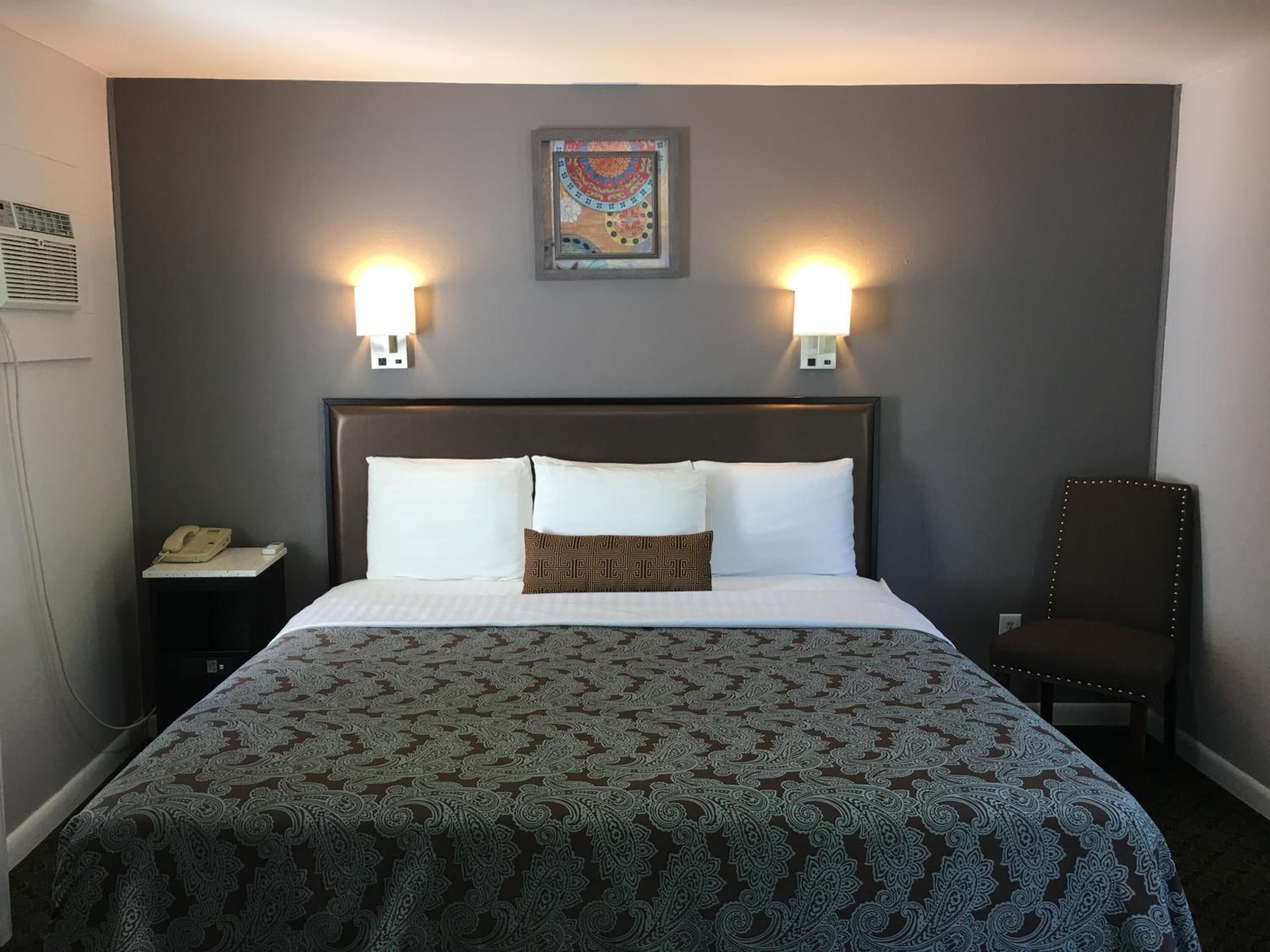A hotel room with a large bed, two bedside lamps, a chair, and a telephone on a nightstand.