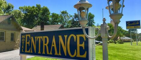 A motel entrance sign with a clear sky and a Scottish Inns sign in the background.