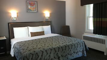A neatly made bed with a patterned bedspread, two wall-mounted lights, a decorative wall hanging, and a window with curtains.