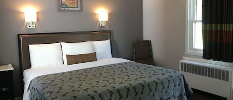 A neatly made bed with a patterned bedspread, two wall-mounted lights, a decorative wall hanging, and a window with curtains.