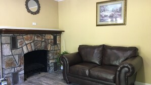 A living room with a stone fireplace, a brown leather sofa, a framed picture on the wall, and a small plant. - Scottish Inns Milford (Milford)