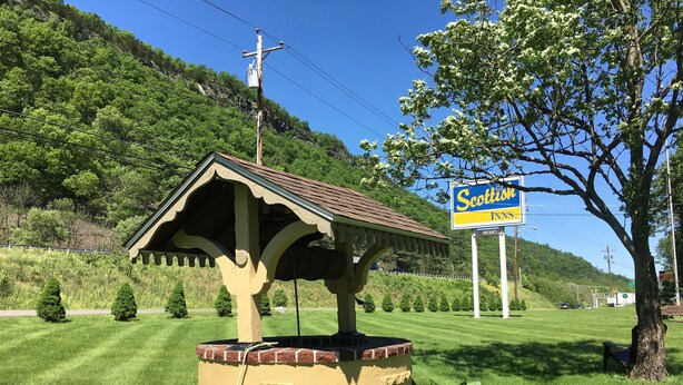 A small, standalone structure with a pitched roof, possibly a gazebo or shelter, surrounded by well-maintained grass and plants. In the background, there is a sign for 'Scottish Inns' indicating the presence of a hotel nearby. - Scottish Inns Milford (Milford)