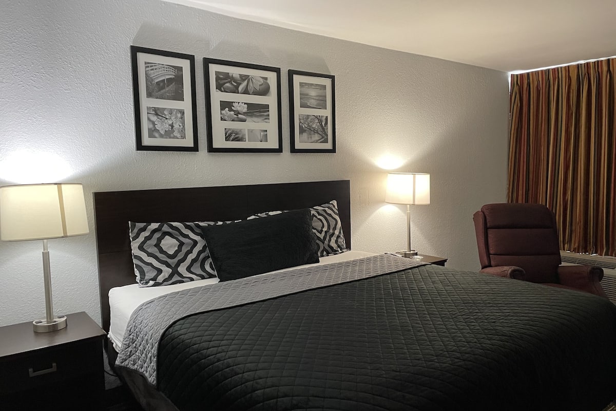 A hotel room with a bed, two bedside lamps, a chair, and three framed pictures on the wall.