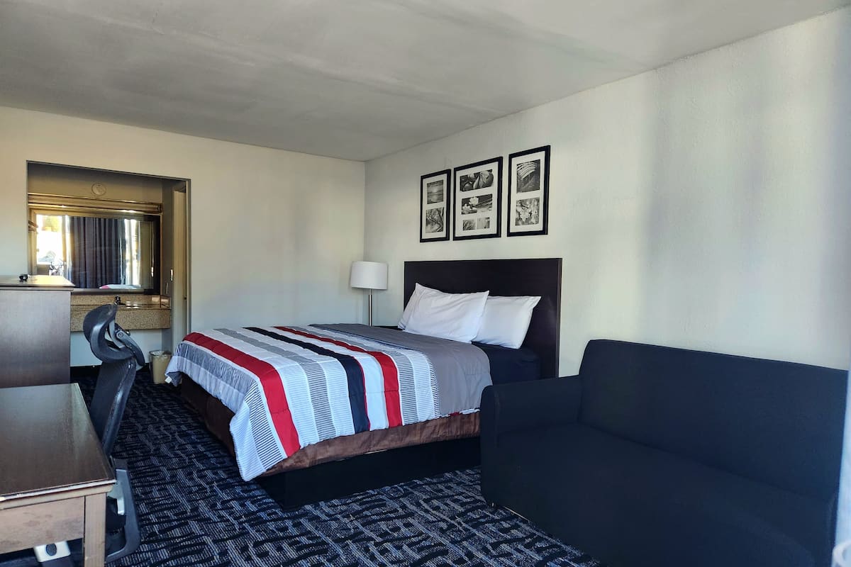 A hotel room with a bed, a desk, a chair, a sofa, and a wall with framed pictures.