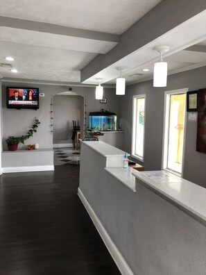 A reception area with a counter, a fish tank, a television displaying news, and a clock on the wall. - Scottish Inn Manchester (Manchester)