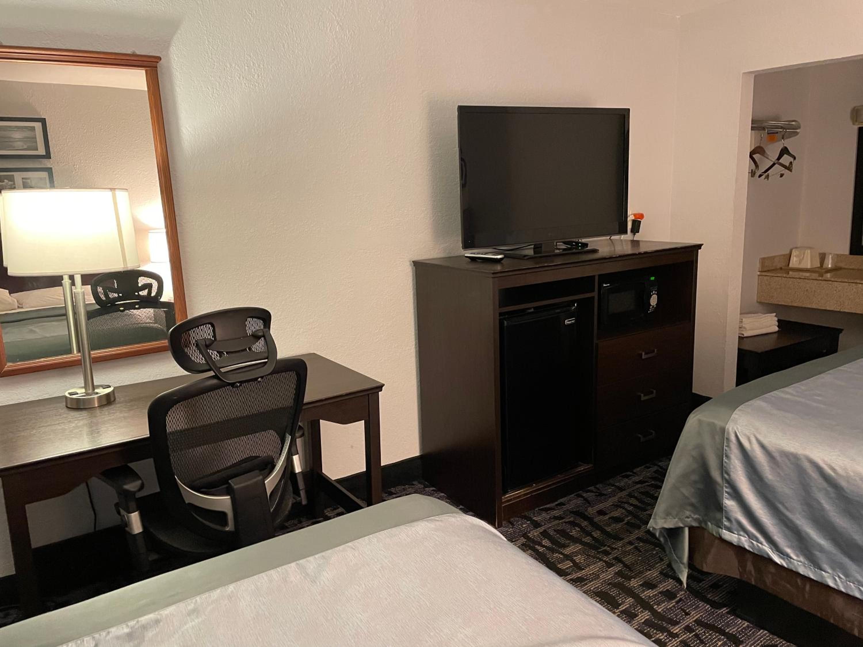 A hotel room with a desk, chair, television, minibar, and two beds.