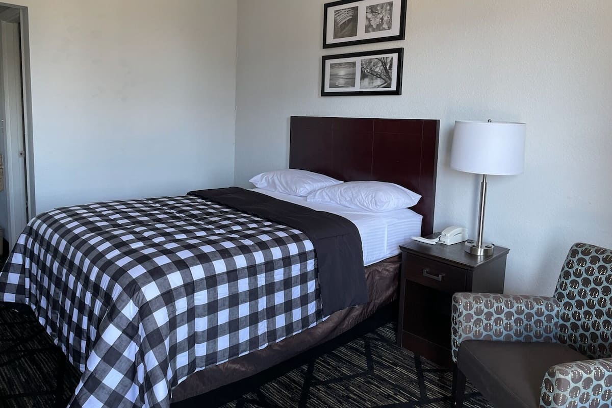A hotel room with a bed, a nightstand, a lamp, and two framed pictures on the wall.