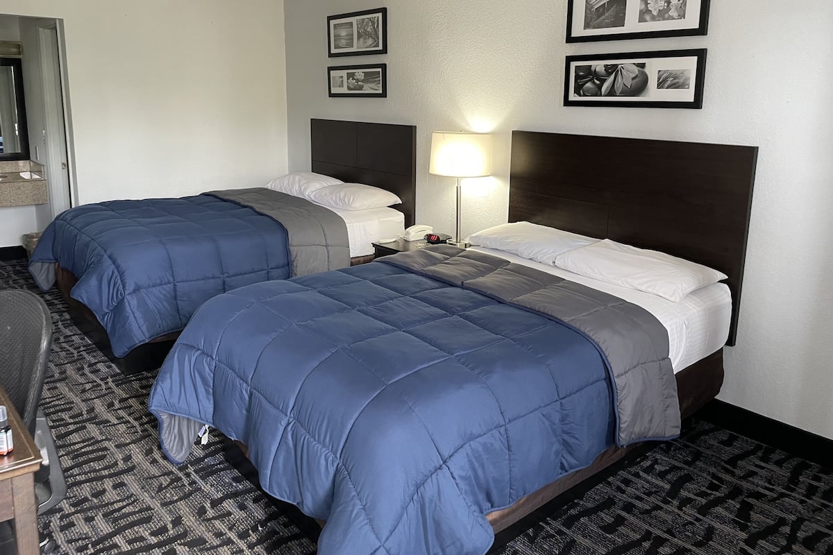 A hotel room with two beds, a desk, and a chair. There are framed pictures on the wall.