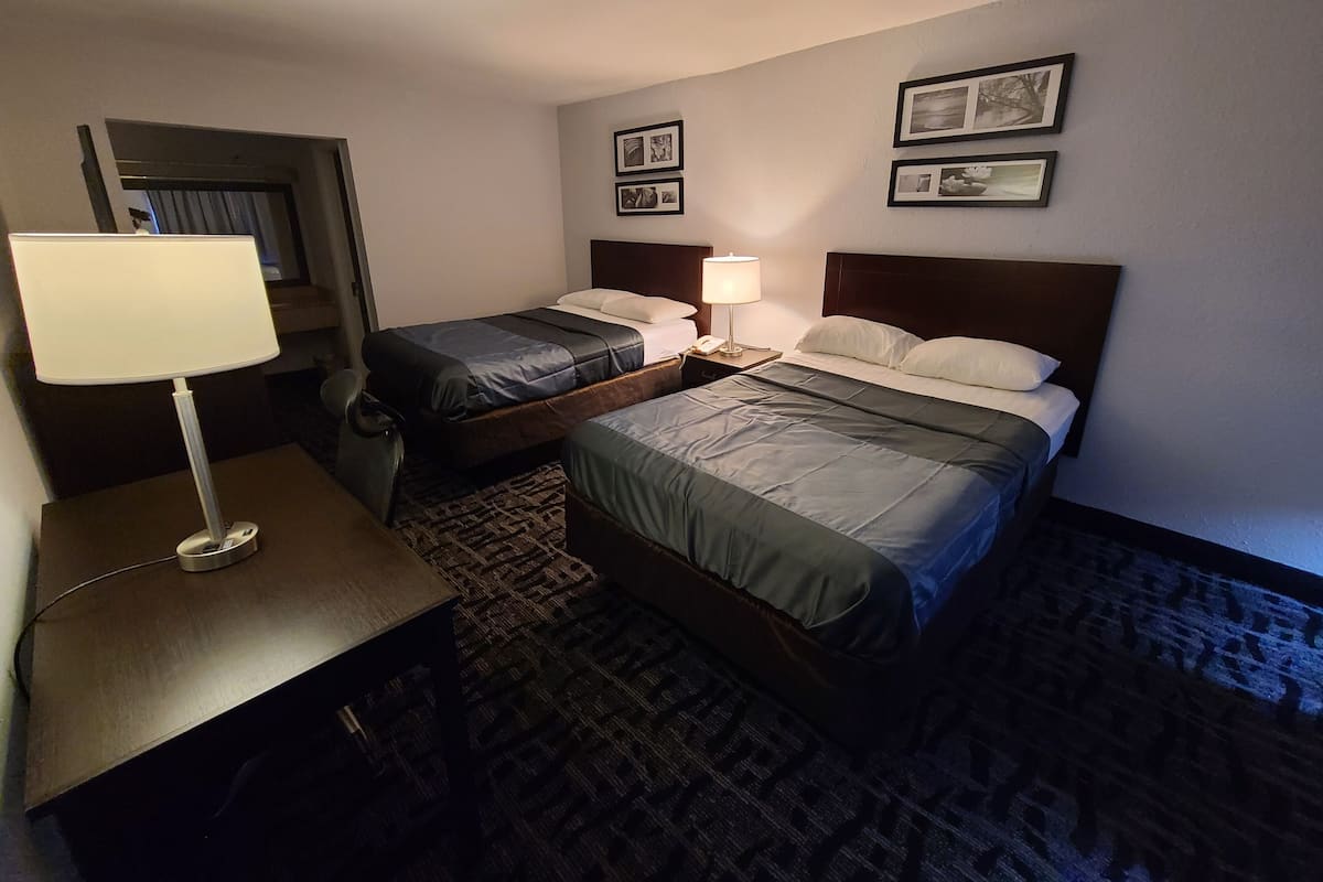 A hotel room with two beds, a desk with a lamp, a telephone, and framed pictures on the wall.