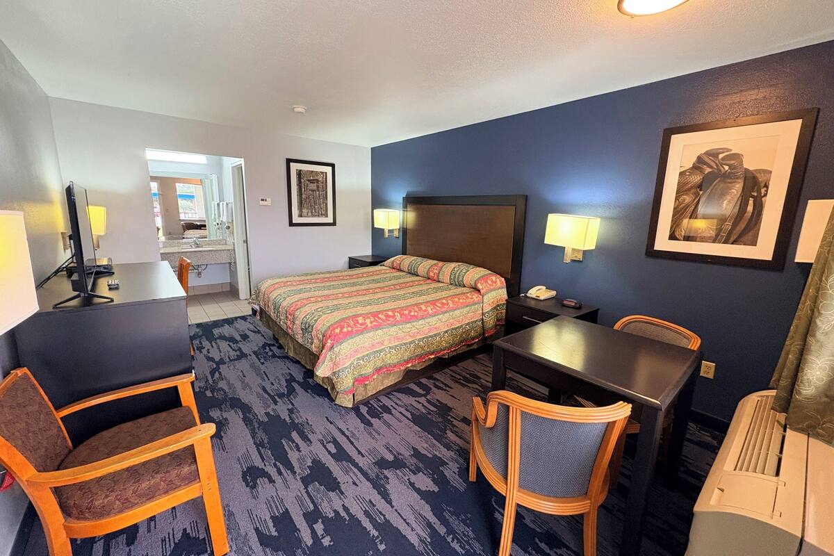 A hotel room with a bed, desk, chairs, and a bathroom visible through an open door.