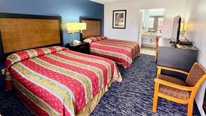 A hotel room with two beds, a desk, a chair, a lamp, and a bathroom visible through an open door. - Scottish Inns Westcott Street (Houston)
