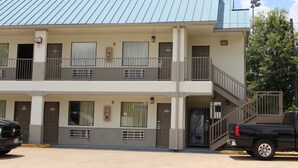 A two-story motel with a metal roof, balconies, and a parking area with a black pickup truck. - Scottish Inns Westcott Street (Houston)