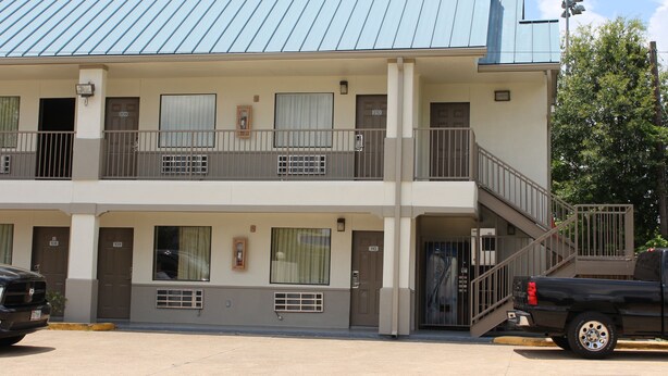 A two-story motel with a metal roof, balconies, and a parking area with a black pickup truck. - Scottish Inns Westcott Street (Houston)