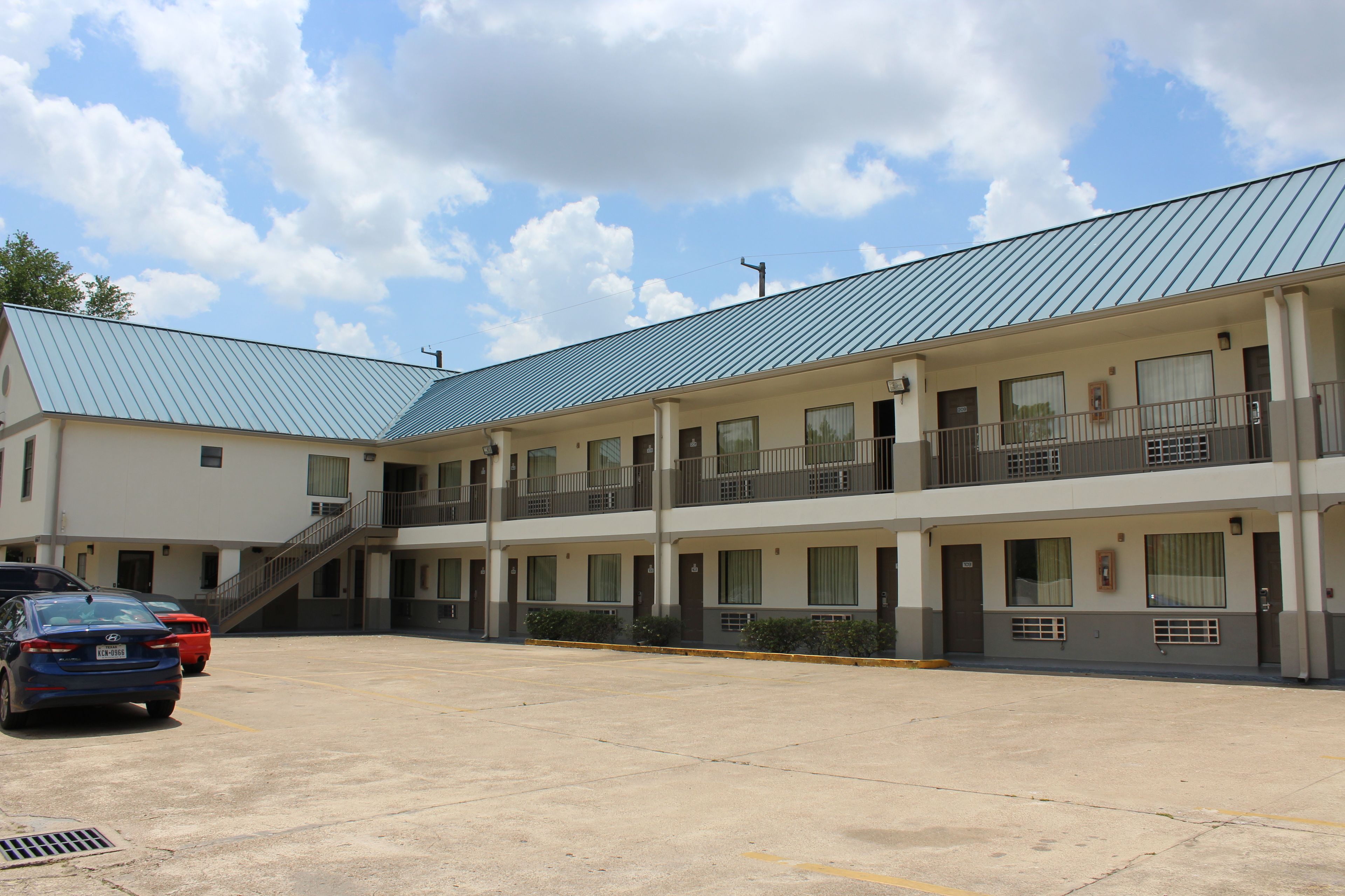 Un motel à plusieurs étages, doté d’un toit plat, de nombreux balcons et d’un parking où sont stationnées plusieurs voitures.