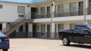 A two-story motel with a covered parking area, a stairway to the upper level, and a black pickup truck parked in the lot. - Scottish Inns Westcott Street (Houston)
