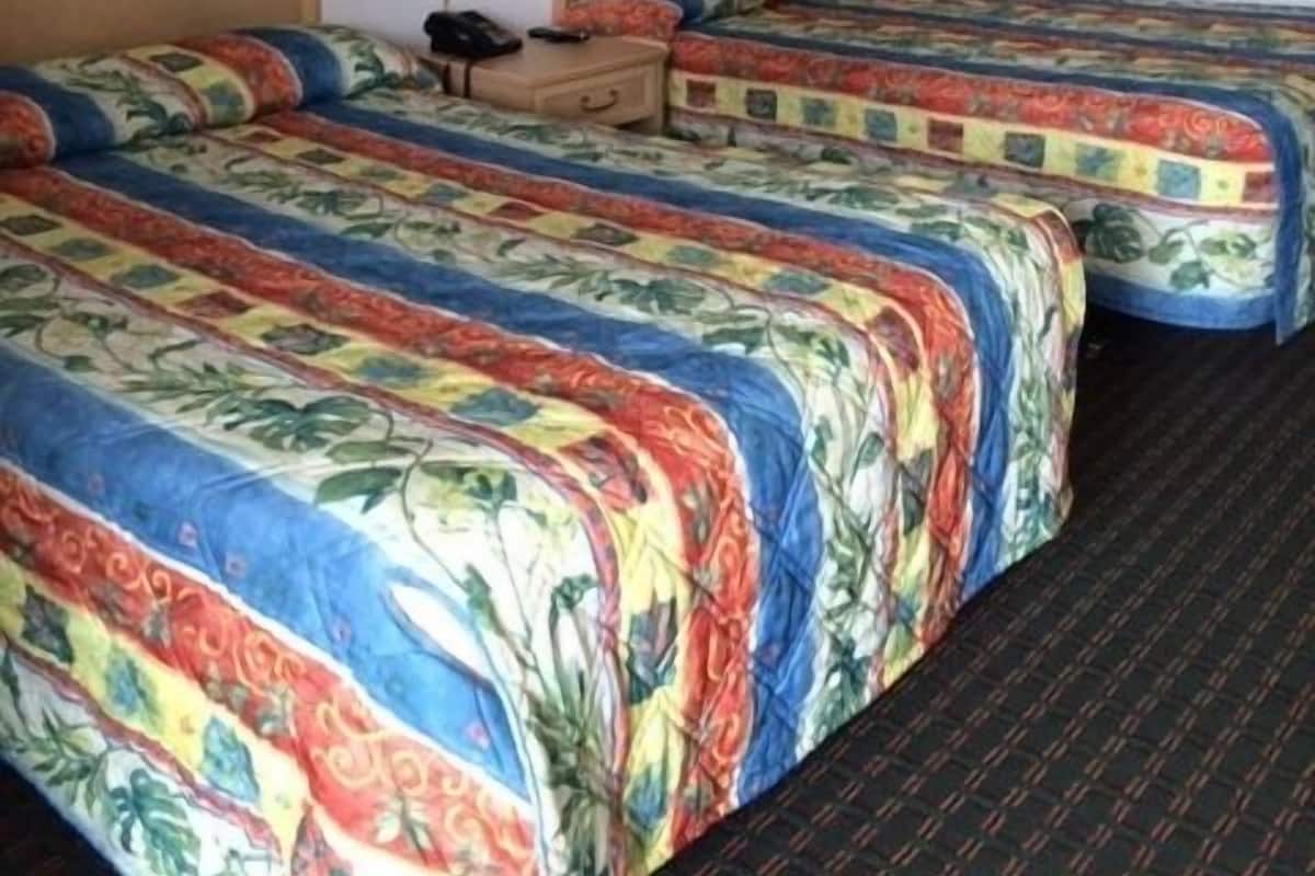 A hotel room with two beds, each with floral-patterned bedding, a nightstand with a lamp, and wall-mounted artwork.