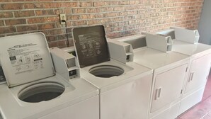 A row of white laundry machines with instructions and a brick wall in the background.