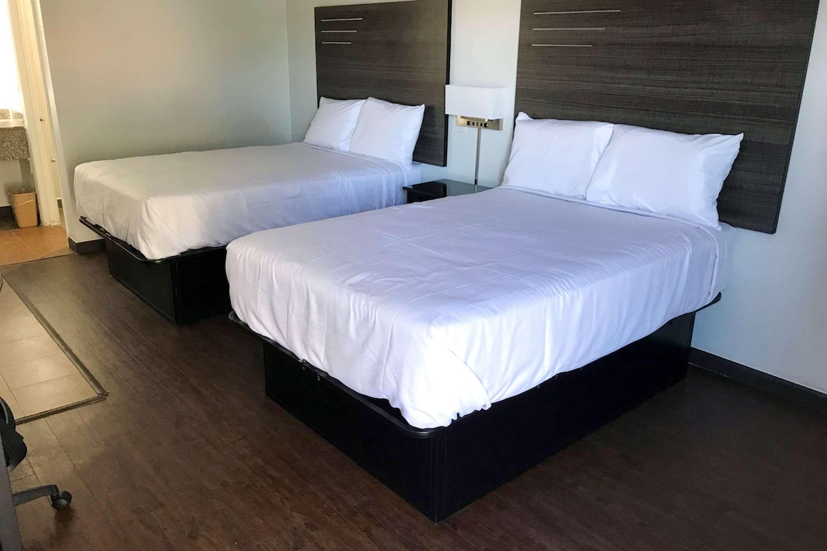 A hotel room with two single beds, a desk, and a chair.
