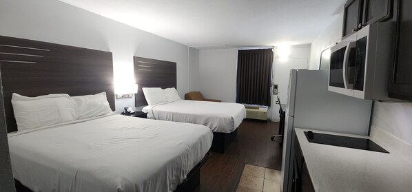 A hotel room with two beds, a desk, a chair, a microwave, and a refrigerator.