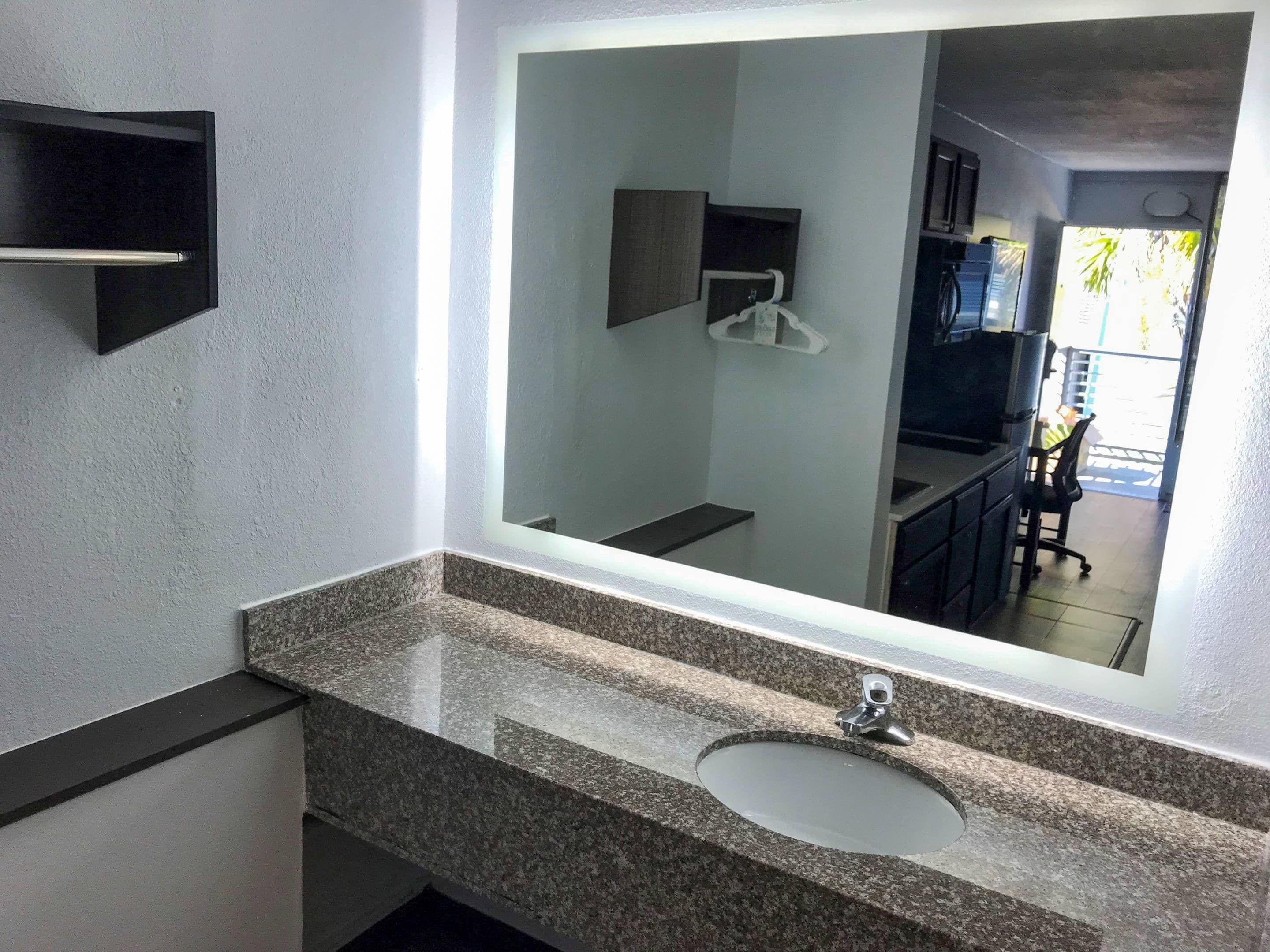 Un baño con un espejo grande, una encimera de granito y un lavamanos.