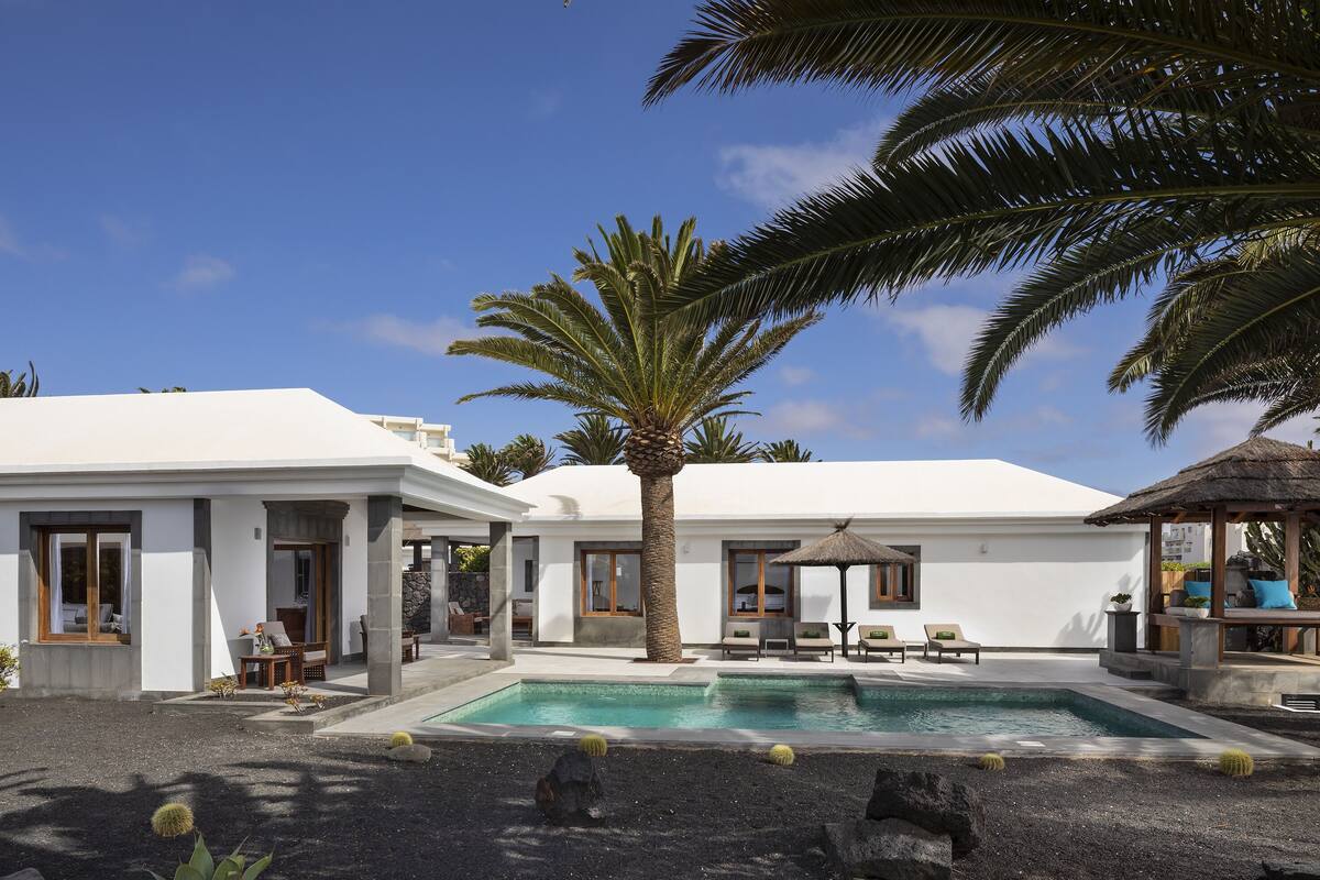 A modern resort with a pool, palm trees, and a thatched-roof gazebo.