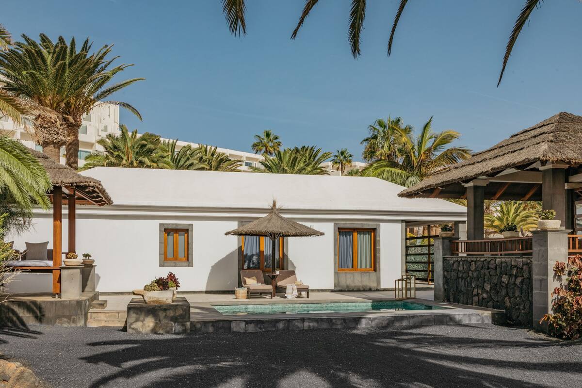 A pool area with lounge chairs, a thatched umbrella, and a stone wall.