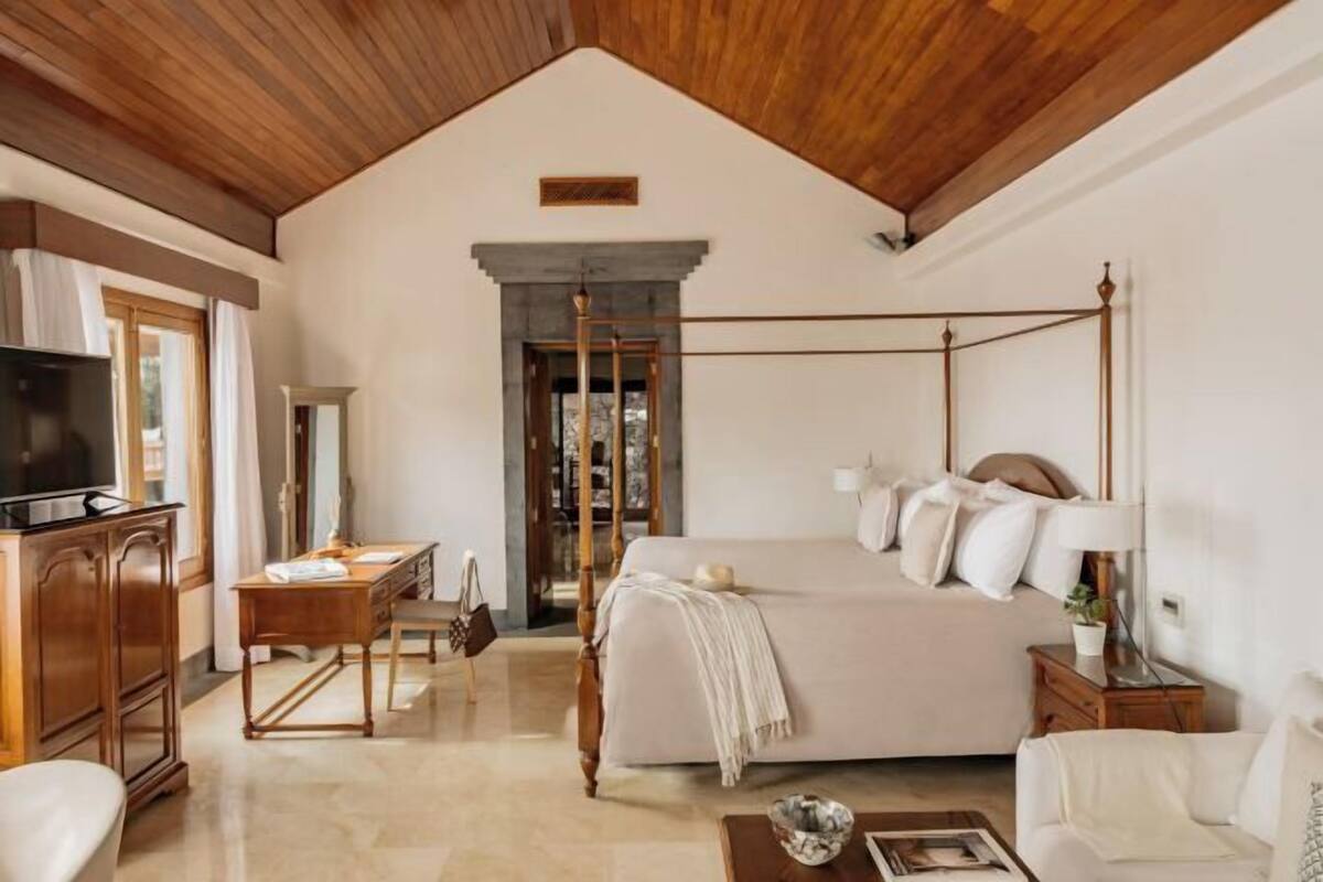 A bedroom with a four-poster bed, a television, a desk, and a chair.