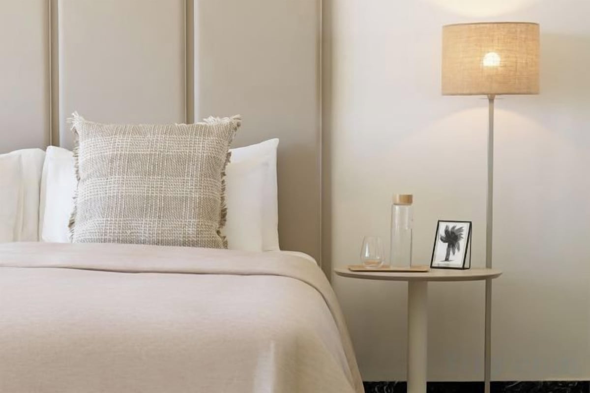 A neatly made bed with a textured pillow, a bedside table with a lamp, and a framed picture.
